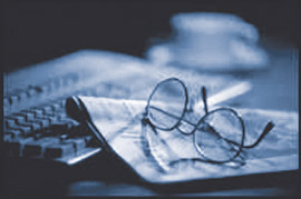 image of reading glasses sitting on top of a newspaper and a computer keyboard in the background